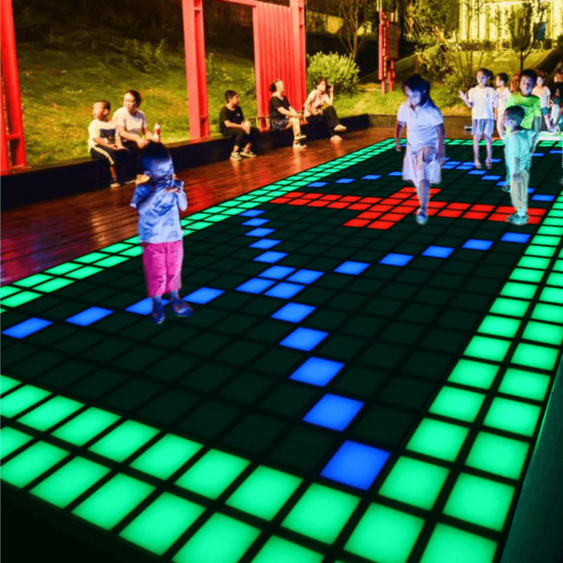 Children playing on a large illuminated grid with colorful lights in an outdoor setting.