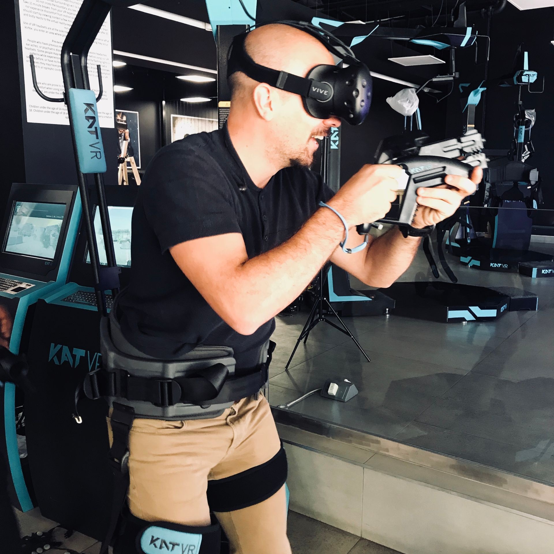 Person using VR headset and gear in a gaming center, holding a VR gun controller.